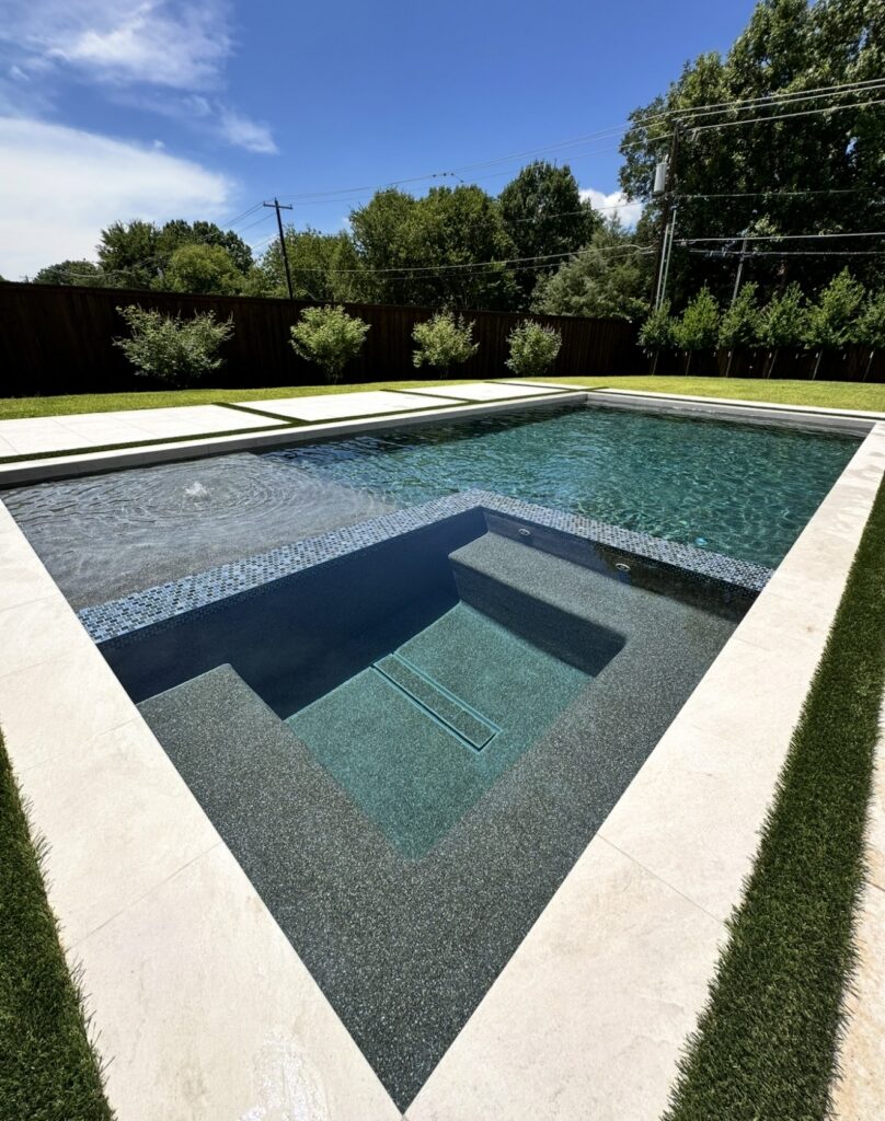 Clean backyard swimming pool with attached spa, waterfall, and shallow lounging area
